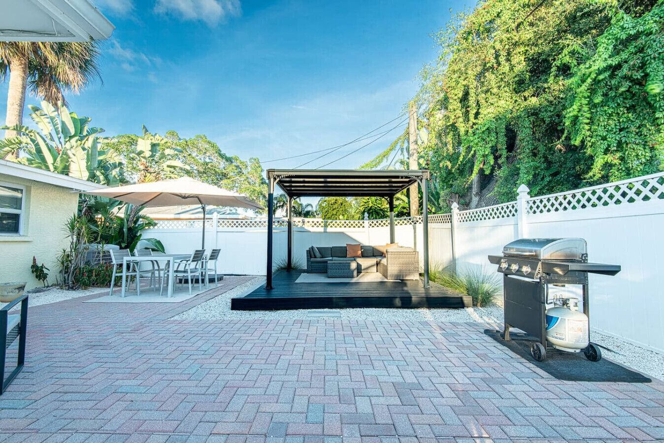 A covered patio area with outdoor furniture, a grill, and a white fence.