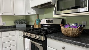 A kitchen with white cabinets, a gas stove, a microwave, and a basket of snacks on the countertop. - Capeside Cottage (La Crosse)