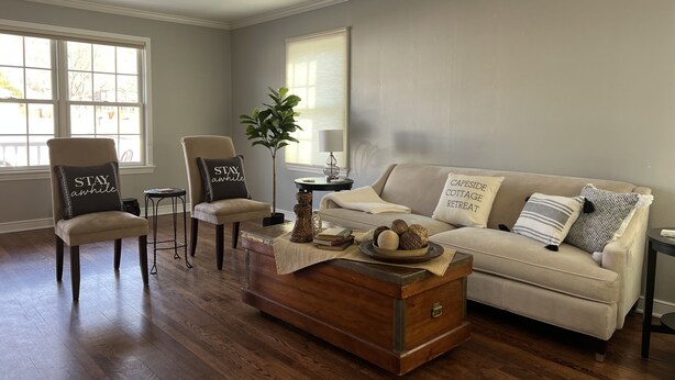 A living room with a beige sofa, two armchairs, a wooden coffee table, and a potted plant. - Capeside Cottage (La Crosse)