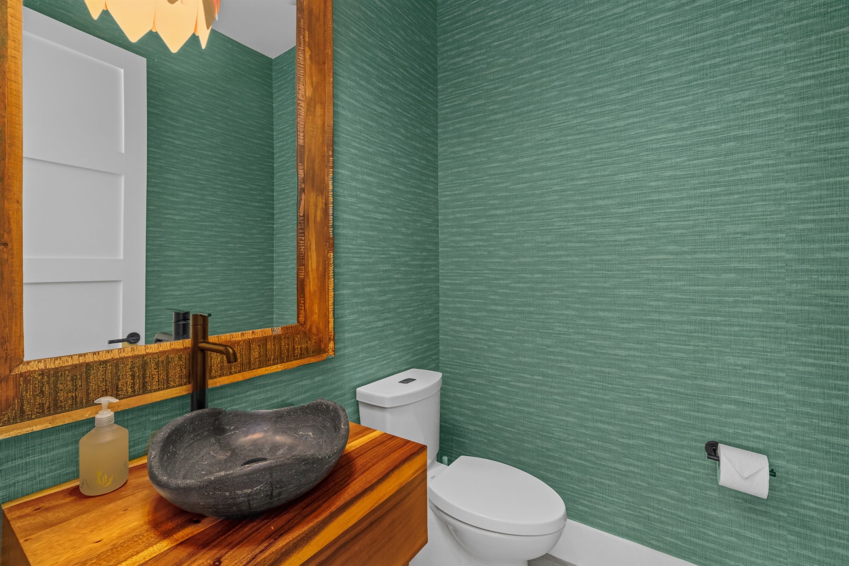 Een badkamer met een houten wastafelmeubel, een stenen wastafel, een wit toilet en groene, gestructureerde wanden.