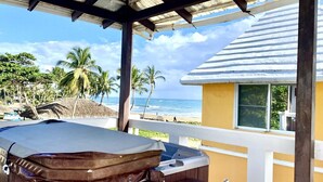 Un espacio al aire libre cubierto con un jacuzzi, vista a la playa y palmeras.