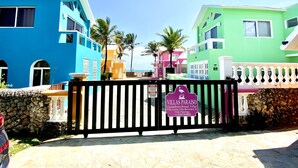 Una entrada vigilada a un resort colorido con un cartel que indica 'Villas Paraiso Oceanfront Rental Villas'.