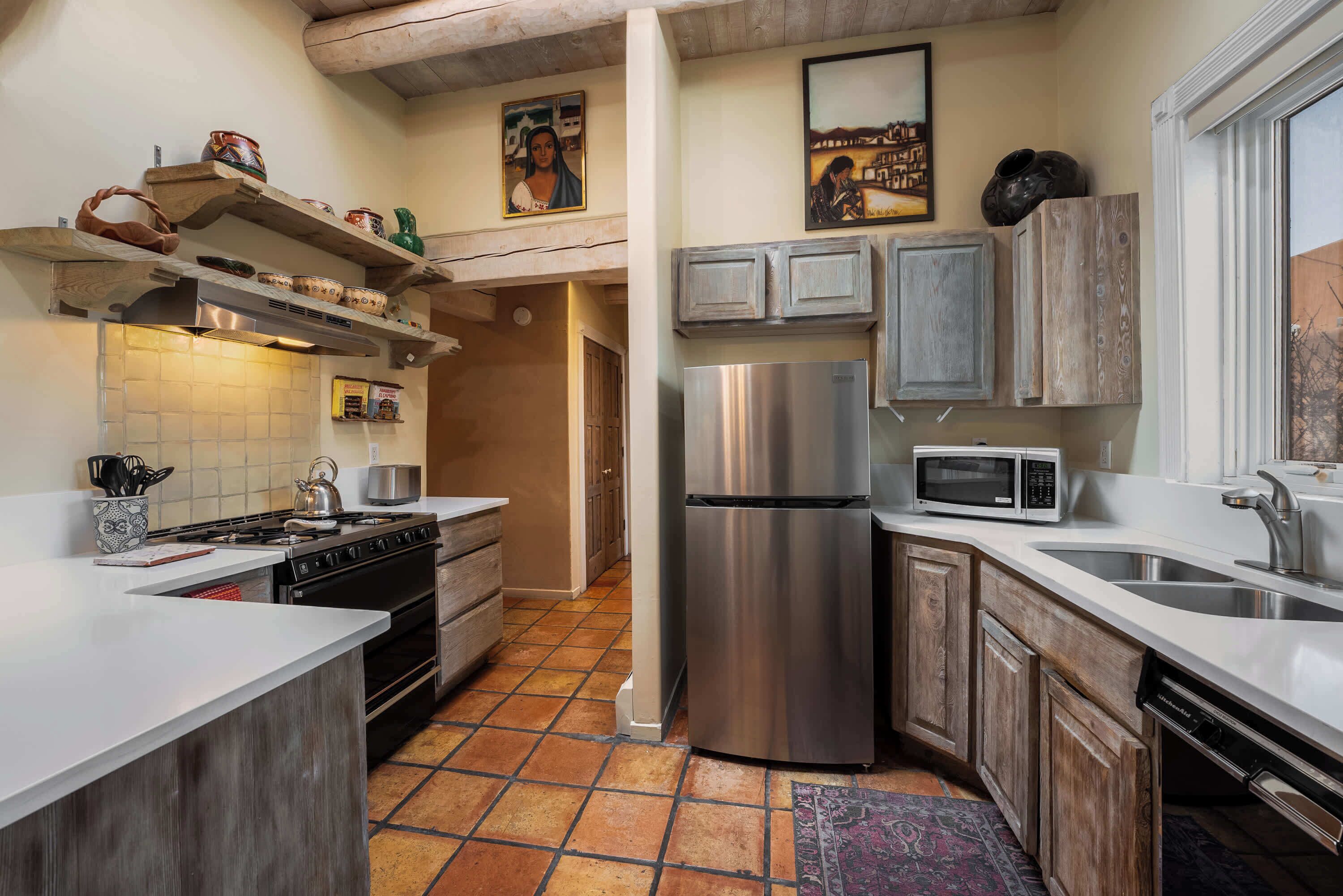 Una cocina moderna con refrigerador de acero inoxidable, microondas y estufa. Cuenta con gabinetes de madera y un salpicadero de azulejos.