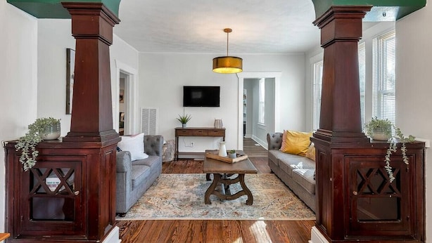 Un salon avec un plancher en bois, un ensemble de canapés, une table basse et un téléviseur fixé au mur.