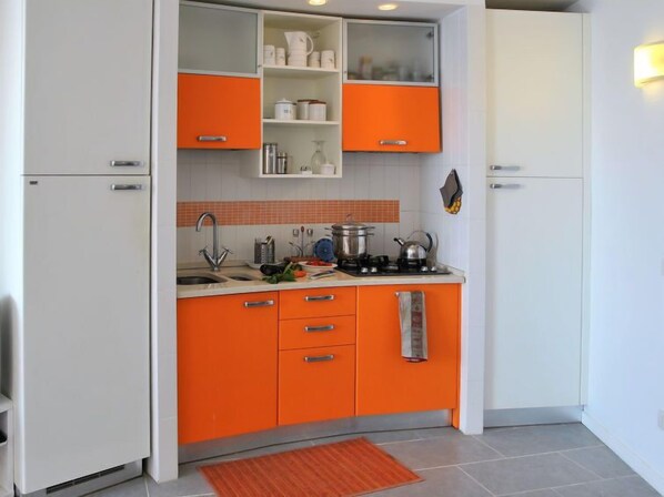 A compact kitchen with orange cabinets, a white refrigerator, and a tiled backsplash.