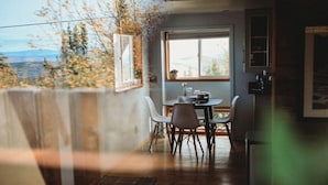 A dining area with a table and chairs, a window with a view of trees and mountains, and a wooden floor.