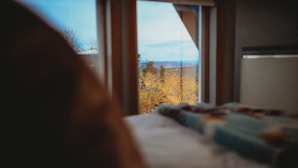 A bedroom with a window overlooking a landscape with trees and a distant view.