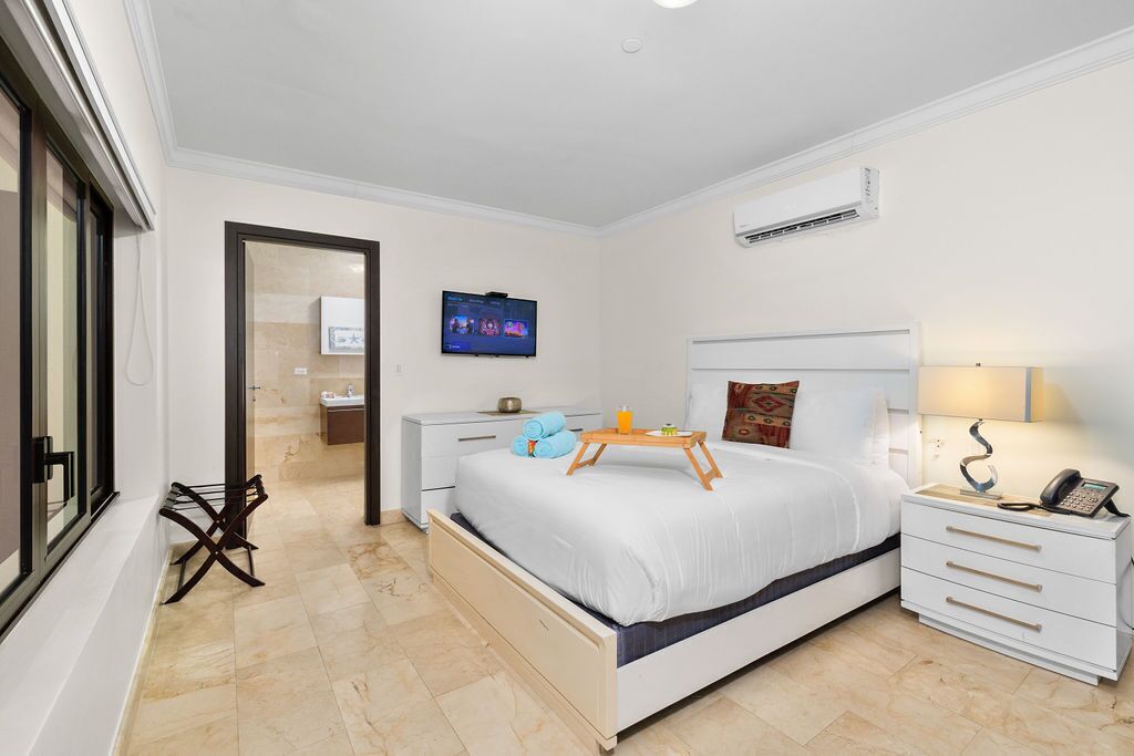 Una habitación de hotel moderna con cama, mesita de noche, televisor y aire acondicionado.