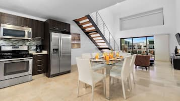 Eine moderne Küche mit Edelstahlgeräten, eine Essecke mit einem Glastisch und eine Treppe, die zu einer oberen Ebene führt.