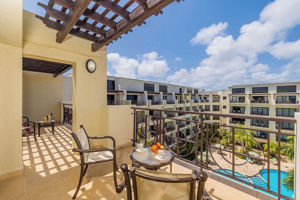 Ein Balkon mit Blick auf einen Pool, einer Pergola und einem Tisch mit Obst und einer Tasse.