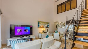 Ein modernes Wohnzimmer mit Flachbildfernseher, einem weißen Sofa, einem Essbereich und einer Treppe.