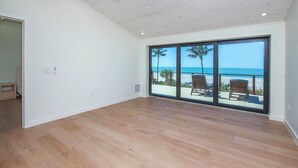 A spacious room with a large sliding glass door leading to a balcony with a view of the beach.