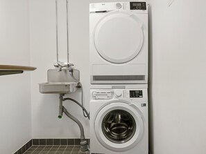 A compact, wall-mounted washing machine with a control panel, a small sink, and a hose.