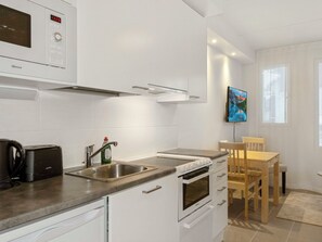 Una cocina moderna con armarios blancos, microondas integrado, cafetera y un comedor con mesa y sillas de madera.