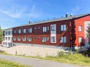 A multi-story residential building with a red facade, multiple windows, and a gravel driveway.