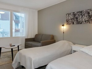 A hotel room with two beds, a sofa, a small table, and a window with blinds.