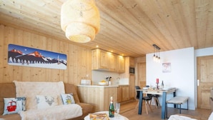 L’intérieur chaleureux d’un chalet avec un plafond en bois, un coin repas et un salon comprenant un canapé et une petite table.