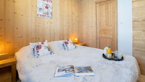 Une pièce chaleureuse aux murs en bois, un lit avec une literie blanche, une affiche accrochée au mur et un plateau de petit-déjeuner posé sur le lit.
