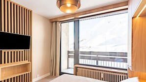 Une chambre moderne avec un grand lit, un téléviseur intégré, un lambris en bois et une vue sur un paysage enneigé par une grande fenêtre.