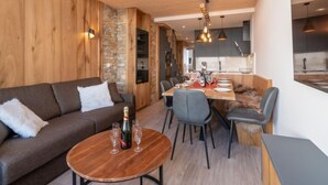 Un salon moderne avec un mur en bois, un mur d’accent en pierre, un coin repas avec une table et des chaises en bois, et une cuisine en arrière-plan.