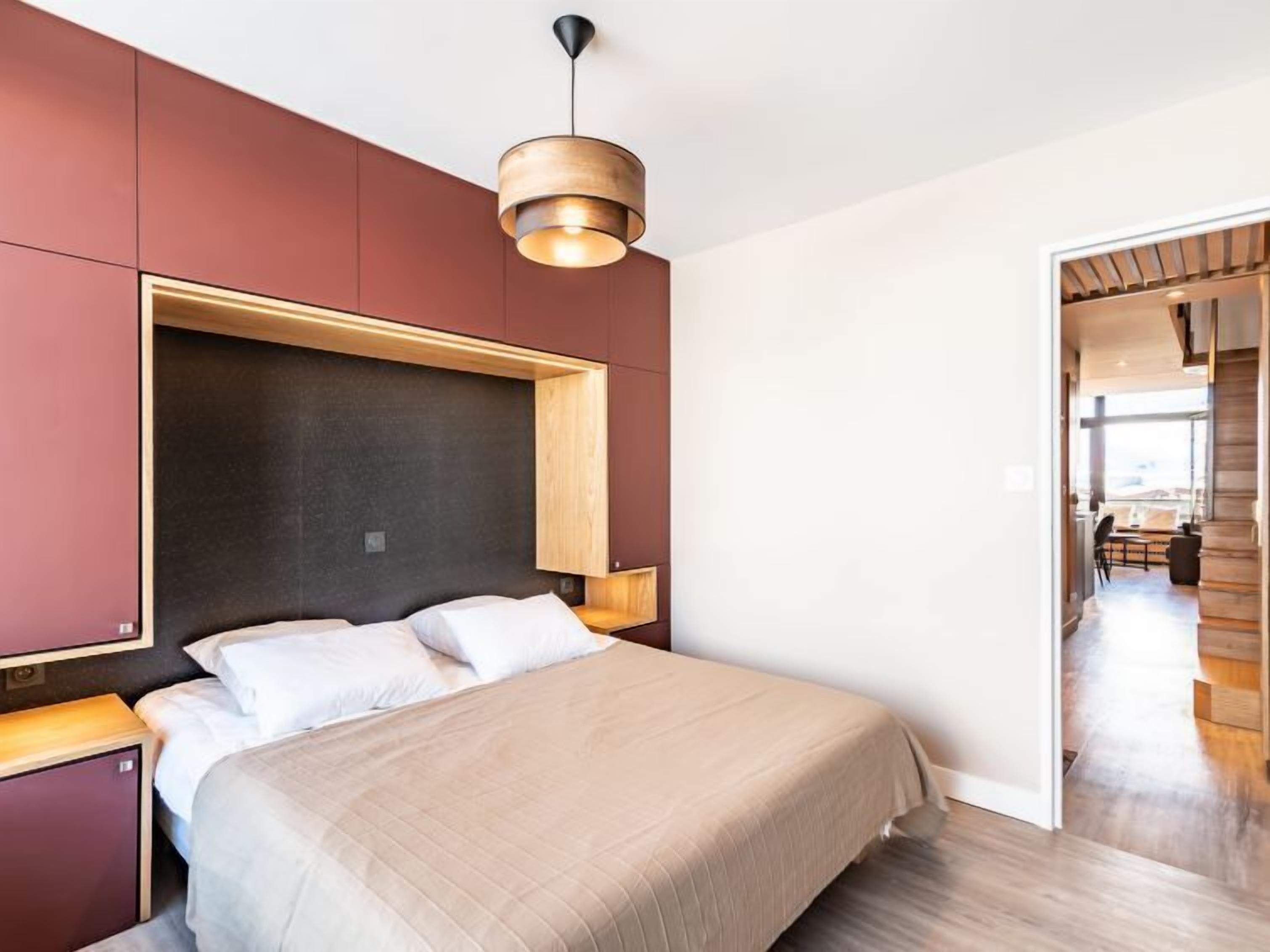 Une chambre moderne avec un grand lit, une tête de lit en bois et un luminaire suspendu.