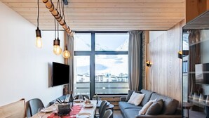 Un espace repas moderne avec une table en bois dressée pour un repas, un canapé et une grande fenêtre offrant une vue sur les montagnes.