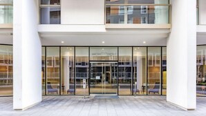 Ingresso moderno di un hotel con porte in vetro e una zona salotto esterna coperta.