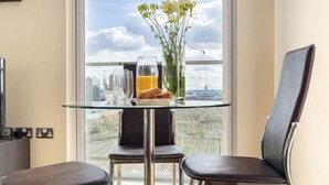 Zona pranzo moderna con tavolo in vetro, due sedie nere, un vaso con fiori gialli, un bicchiere di succo d'arancia e un cornetto.