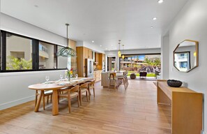 A modern kitchen with wooden cabinets, a dining area with a round table, and a view of a waterfall and pool outside.