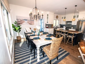 Una cocina moderna con armarios blancos, un refrigerador de acero inoxidable y un comedor con candelabro y sillas de mimbre.