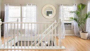 A staircase with a white railing, a round mirror on the wall, and a potted plant. - Juniper Cottage | Houston (Houston)