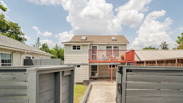 A residential backyard with a house, a wooden fence, and a red balcony. - Juniper Cottage | Houston (Houston)