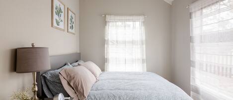 A bedroom with a bed, a bedside table with a lamp, a clock, and framed botanical prints on the wall.