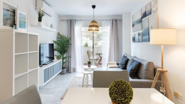 A modern living room with a sofa, TV, and a dining table with a potted plant. - APARTMENT MONKÓ GOLF & BEACH (Benalmadena)
