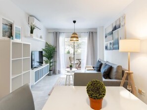 A modern living room with a sofa, TV, and a dining table with a potted plant.
