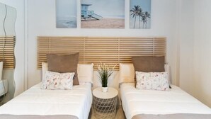 A hotel room with two beds, a round side table, and three wall-mounted pictures depicting beach scenes. - APARTMENT MONKÓ GOLF & BEACH (Benalmadena)