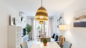 A modern dining area with a white table, grey chairs, a hanging woven light fixture, and a view of the outdoors through a large window. - APARTMENT MONKÓ GOLF & BEACH (Benalmadena)