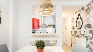A modern dining area with a white table, a potted plant, and a kitchen visible through an open door. - APARTMENT MONKÓ GOLF & BEACH (Benalmadena)