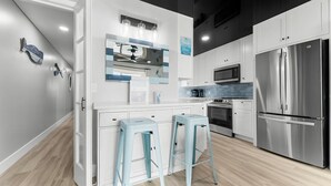 Una cocina moderna con armarios blancos, un refrigerador de acero inoxidable y dos taburetes de color azul claro.