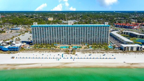 Un hotel grande con varios pisos, piscina y zona de playa con sombrillas.