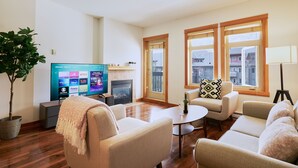 Een woonkamer met een flatscreen televisie, een open haard en een groot raam met uitzicht op gebouwen.