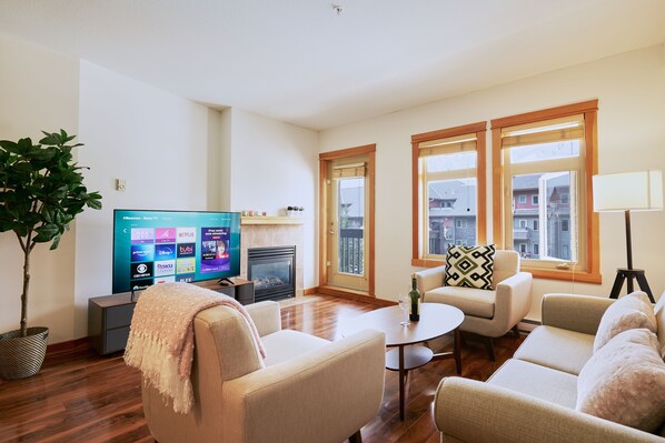 A living room with a flat-screen TV, a fireplace, and a large window with a view of buildings.