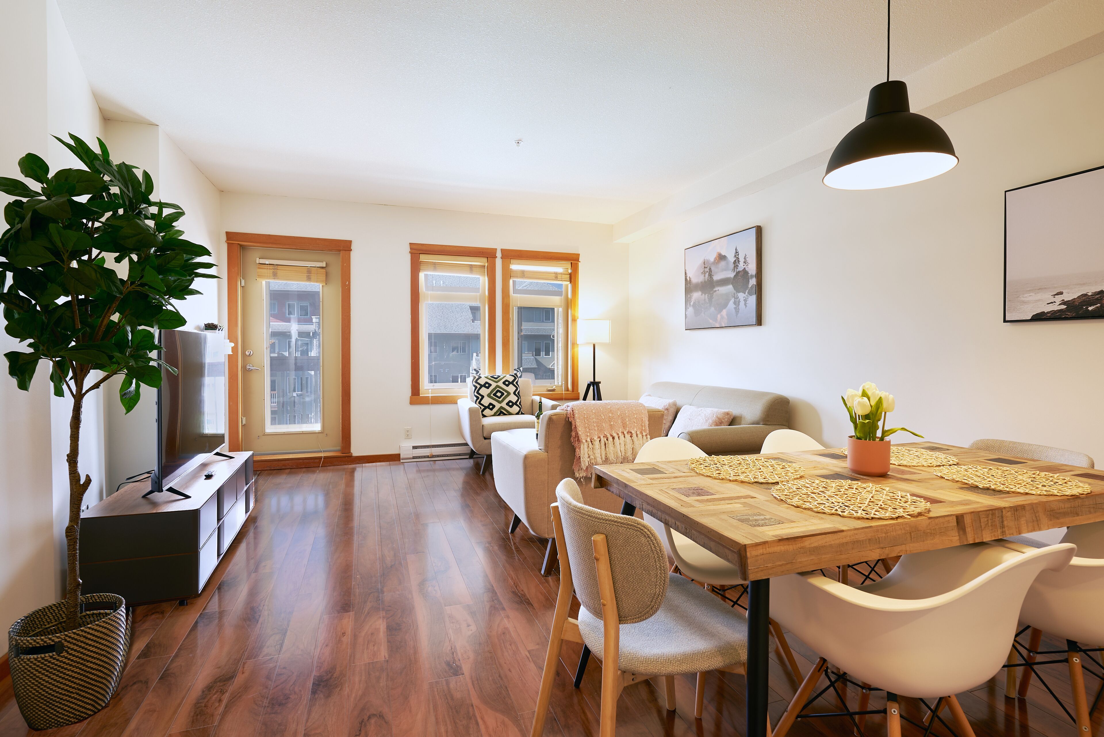 A dining area with a wooden table, white chairs, and a hanging pendant light.