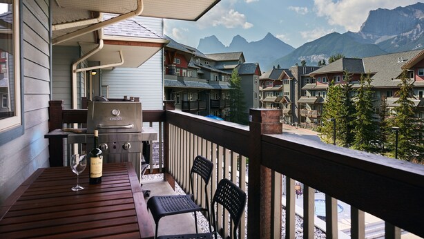 Een balkon met een barbecue, zitplaatsen buiten en uitzicht op huisjes in de bergen.
