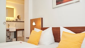 Une chambre d’hôtel comprenant un lit, une tête de lit en bois, une table de chevet, un miroir, un lavabo et un porte-serviettes.