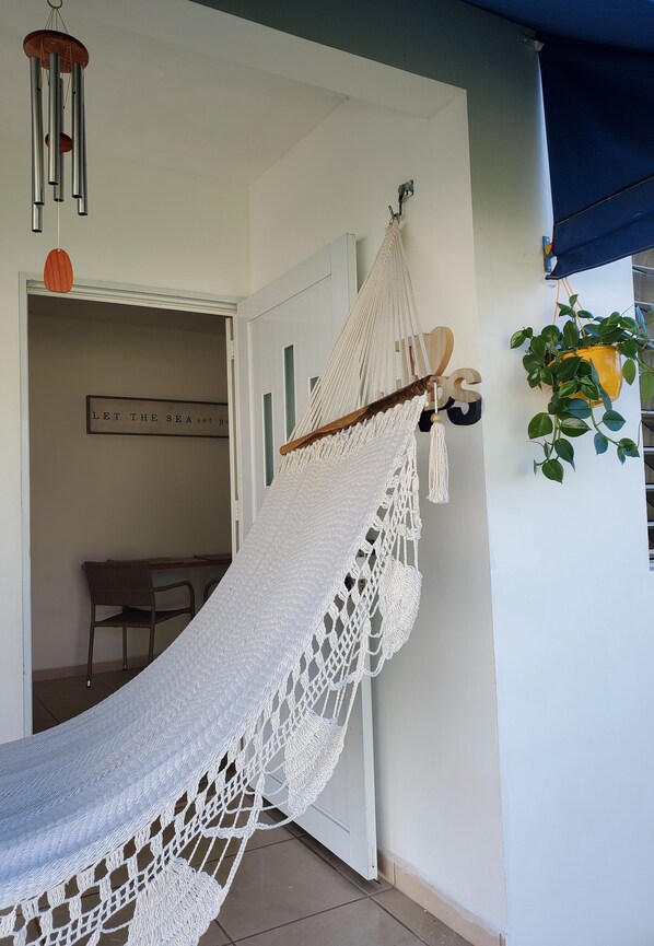 A hammock hanging from a ceiling hook in a room with a white door and a sign on the wall.