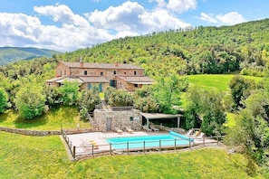 Uma casa de pedra rústica com piscina, rodeada por vegetação exuberante e colinas.