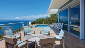 En moderne udendørs terrasse med pool, liggestole og havudsigt.