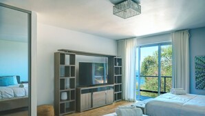 Et moderne soveværelse med stort fjernsyn, indbyggede hylder, to senge og en balkon med udsigt.