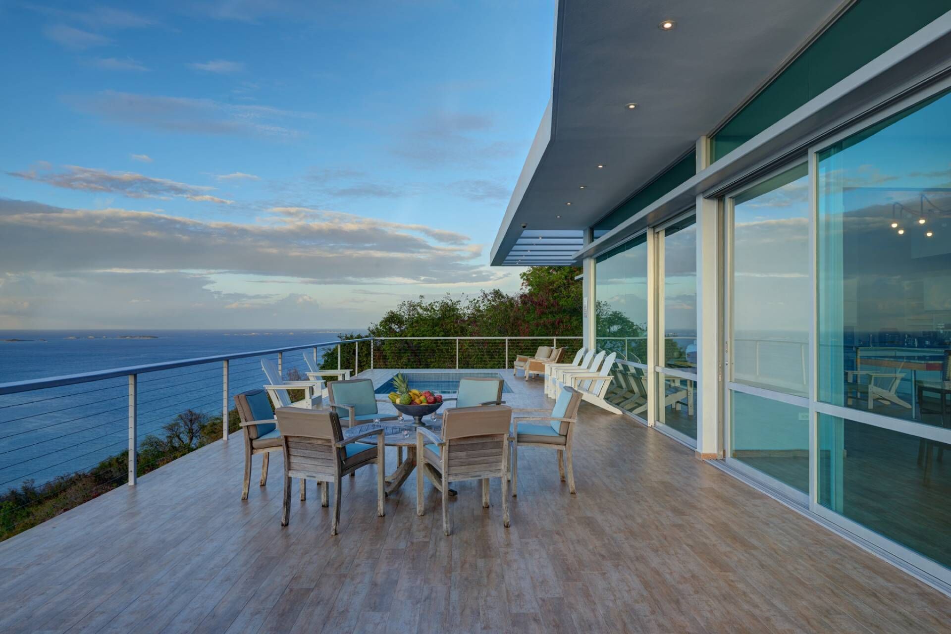 A modern outdoor deck with a pool, lounge chairs, and a view of the ocean.